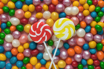 Fototapeta na wymiar Two lollipops on a stick on a background of colorful candy balls. The concept of sweets.