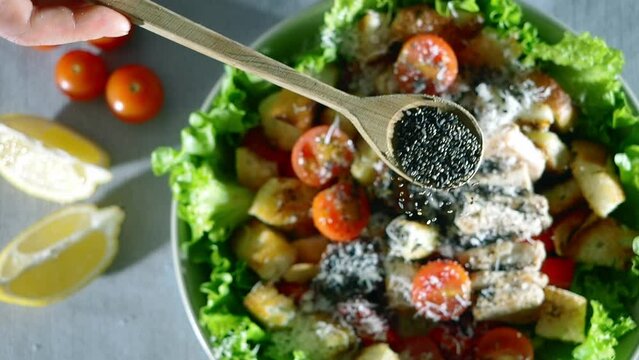 chia seeds falling slow motion, close up video. healthy caesar salad cooking. tomato, chicken. cheese, crunchy croutons, romaine lettuce, olive oil, lemon