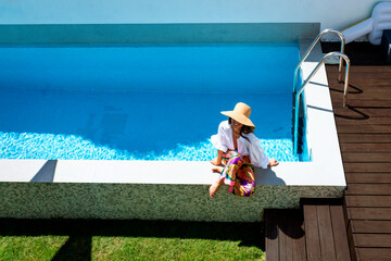 Happy woman wearing white shirt and straw hat while relaxing by the poolside