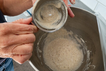 Fototapeta na wymiar Stockholm, Sweden A woman prepares a sourdogh mixture in a baking bowl for baking sourdough bread.