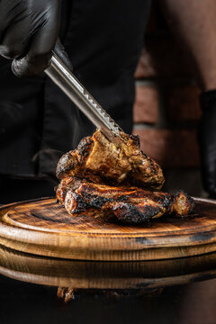 The chef puts fried pork meat on a wooden board on a dark background