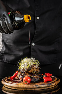 The chef pours sauce over a salad with meat on a dark background