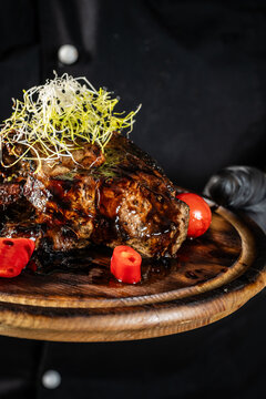 Chef holding a wooden board with a dish of fried pork meat on a dark background