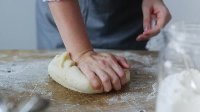Young Woman Baker in Gray Apron Lovingly Kneading Dough on a Wooden Board - Culinary Artistry, Breadmaking, Homemade Baking, and the Joyful Craft of Creating Delicious Treats Cake. Baker knead dough