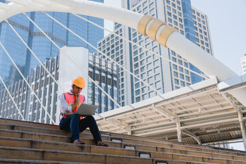 Construction engineer using laptop and sitting outdoor site building working blueprint project, planning project schedule. Thinking problem solving and planning, Engineering and construction concept.