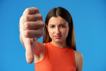 Teen girl over blue background showing thumbs down gesture