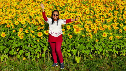 charmant lächelnde Asiatin freut sich in der Natur vor großem blühenden Sonnenblumenfeld
