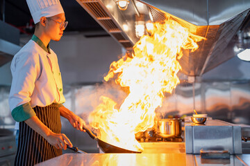 Chef in restaurant kitchen at stove and pan cooking flambe on food