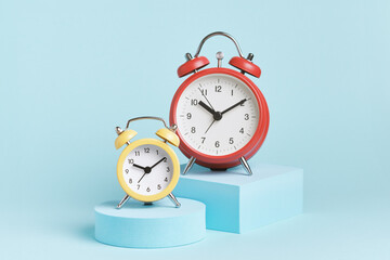 Yellow and red alarm clocks on podiums on a blue background.