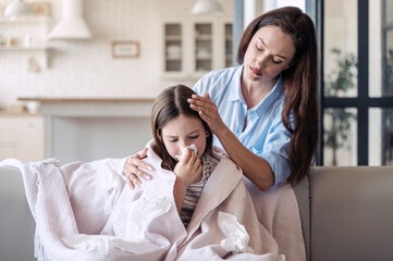 Girl kid feeling bad, has runny nose, using tissue and sitting wrapped in plaid