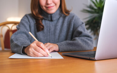Closeup image of a young woman writing on paper while working on laptop computer at home