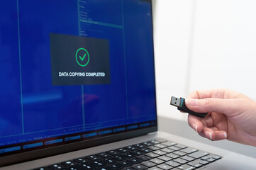 a person holding a usb device in front of a laptop. USB flash drive and laptop - obrazy, fototapety, plakaty