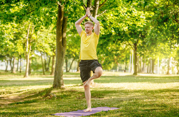 Man practicing yoga standing on one leg outdoors at summer. Guy doing pilates workout for...