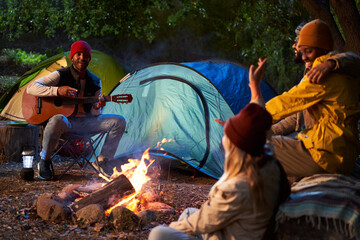 Winter night of group of friends gathered around bonfire playing guitar singing outdoors....