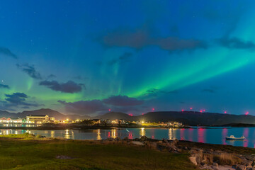 wonderful northern lights over the village of Hillesøya. strong contrast from dark sky with the green Aurora Borealis rising over the clouds, mirroring on fjord, Norway with dancing lady