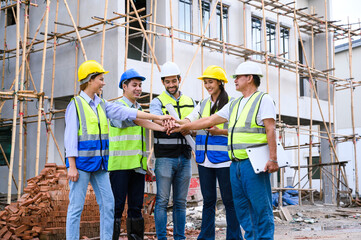 Group of contractors, engineers and formats in safety vests with helmets join hands to work...