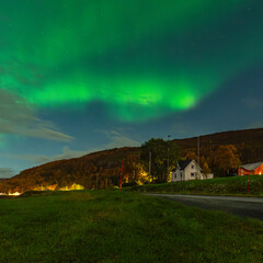 wonderful northern lights over the village of Hillesøya. house on the shore, strong contrast from dark sky with the green Aurora Borealis. autumnal mood in northern Norway with dancing lady