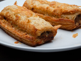 Sausage roll on a white plate, crispy golden flaky pastry