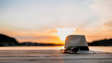 sunset on the sea, hat and sunglasses in backlight on a wooden walkway, the sun reflected in the...