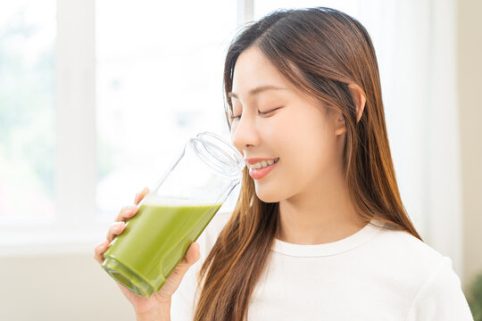 Green detox juice concept, Beautiful smile asian young woman hand holding vegetable smoothie bottle for diet at home. Happy girl drinking healthy meal food for weight loss. Lifestyle, vegan nutrition.
