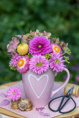 Blumenstrauß mit pink Dahlien, Astern, Strohblumen, Hortensienblüten und einem Apfel in einer...