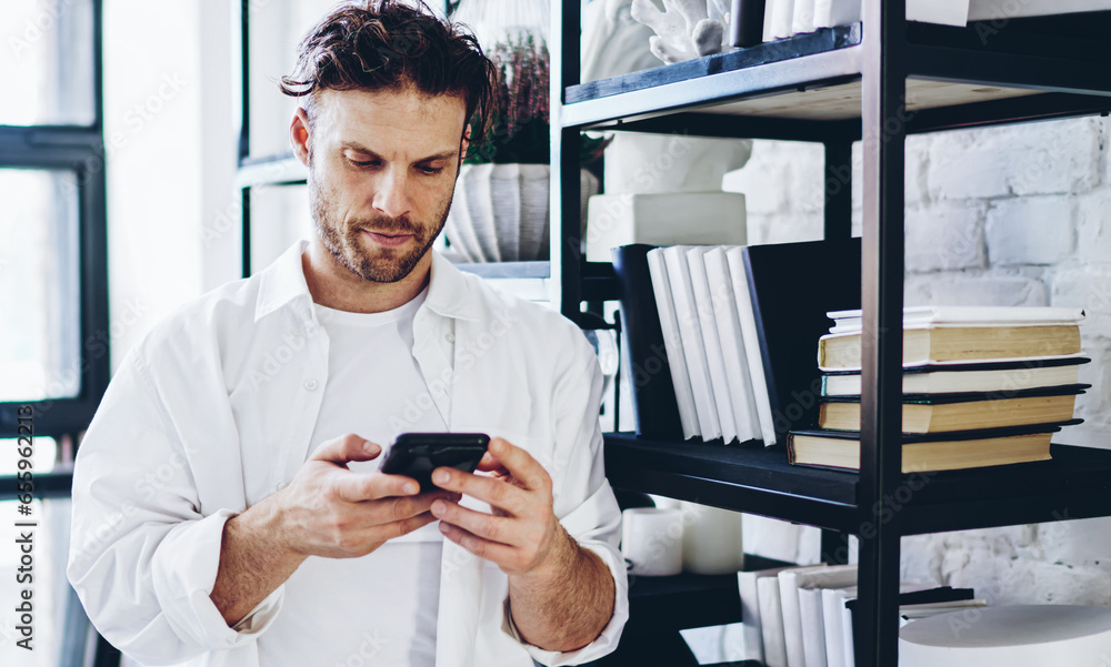 Poster pensive caucasian hipster guy sending text messages via smartphone connected to wifi