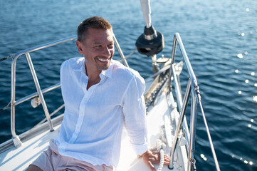 Man in white clothes sitting on a yacht deck and looking relaxed and happy