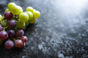 Green and purple organic grapes lie on a dark background. An organic grapes close-up. Fruits on a...