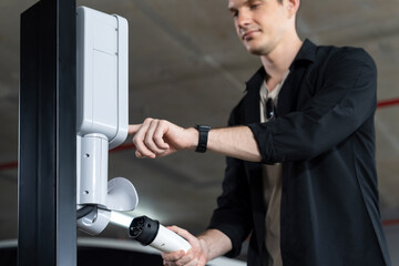 Young man travel with EV electric car to shopping center parking lot charging in downtown city...