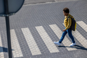 Curly-haired schoolboy crossing the street on a crosswalk