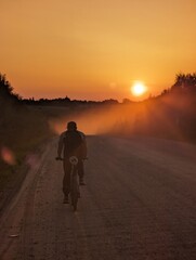 Fototapeta na wymiar Silhouette of a cyclist on a mountain bike riding a trail in a field on a dramatic sunset background. High quality photo