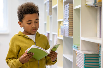 Cute dark-skinned boy in hoodie with a book at school premises