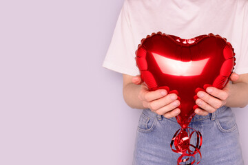 Unrecognizable woman hold in hands red inflatable foil balloon in a heart shape. Concept with copy space in front of blue background.