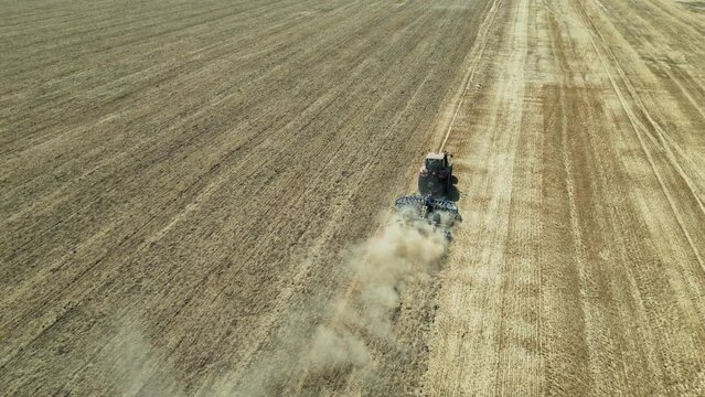 Flying over tractor with harrow system plowing ground on cultivated farm field. Industrial footage on agricultural theme. Agriculture in European country Slovakia. Blue Mountains in the background.