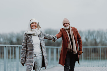 Elegant senior couple walking near the river, during cold winter day.