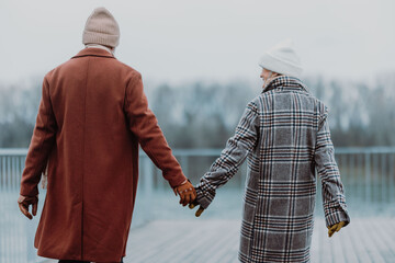 Rear view of senior couple walking near the river, during cold winter day.