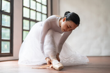 Ballerina in ballet shoes. Asian girl tying ribbons of toe shoes. ballet dancer preparing and wearing ballet shoes in dance studio prepares for a rehearsal.