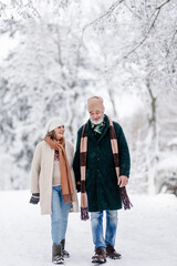Fototapeta na wymiar Elegant senior couple walking in the snowy park, during cold winter snowy day.