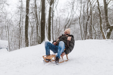 Senior man having fun during cold winter day, sledding down the hill.