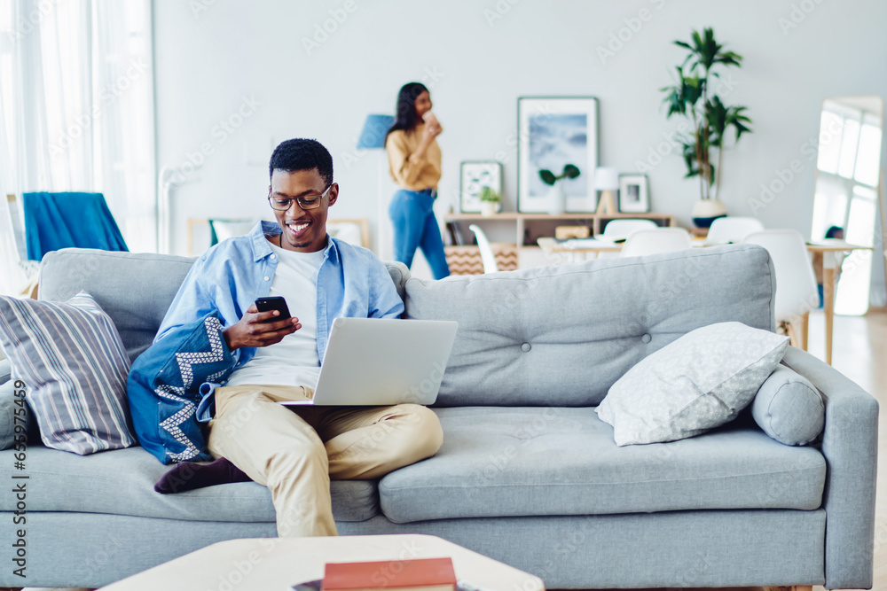 Poster young dark skinned hipster guy using netbook and mobile phone for networking