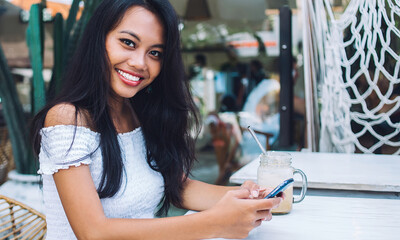 Young Indonesian lady messaging on phone drinking coffee