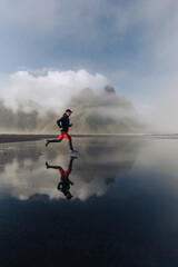 A fit runner is running on the ocean shore in Iceland in cloudy weather.