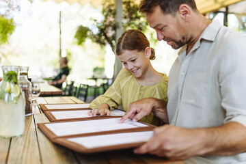 Father and daughter reading menus in a restaurant, choosing food and drinks.