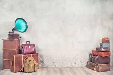 Vintage outdated trunks luggage, old antique leather suitcases pile and classic gramophone front concrete wall background. Travel baggage concept. Retro style filtered photo