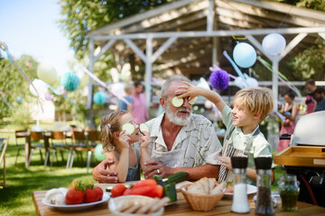 Grandfather and grandchildren having fun at a garden barbecue.