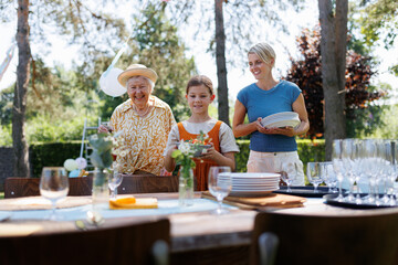 Grandmother, mother and daughter setting table for summer garden party.