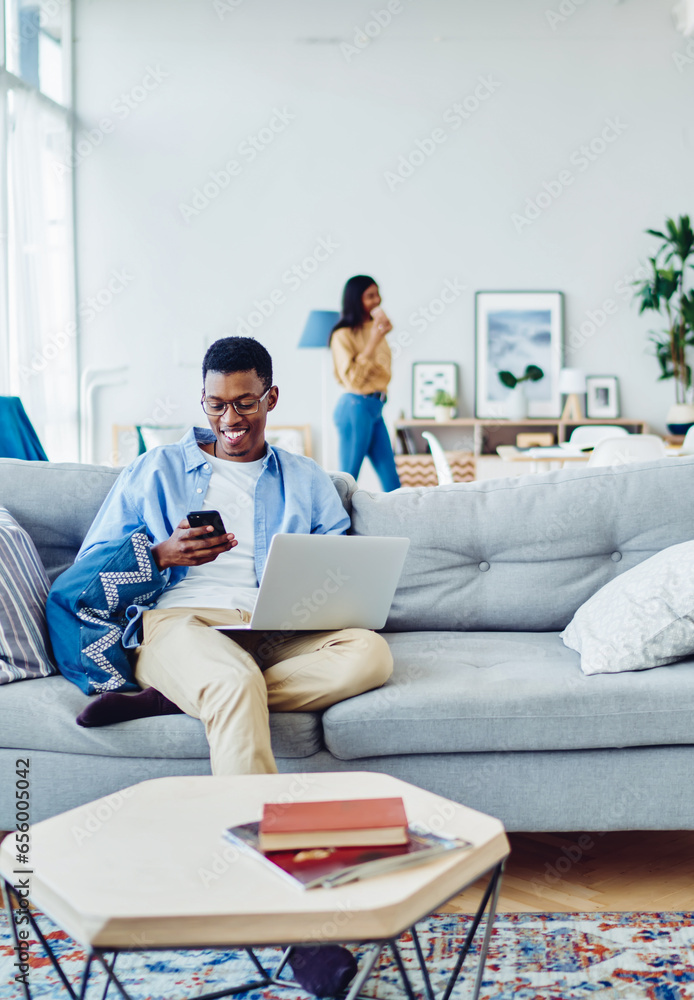 Poster young dark skinned hipster guy using netbook and mobile phone for networking