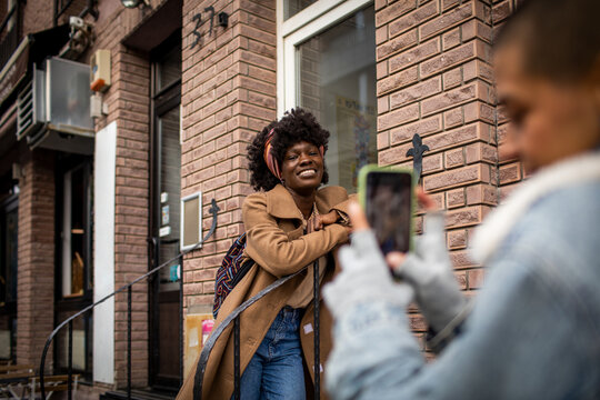 Young African American woman getting her picture taken on a smartphone by her lesbian partner in the city