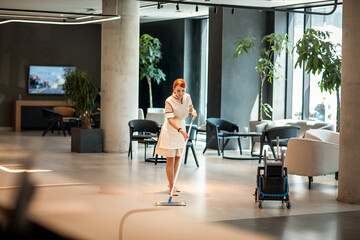 Young cleaning lady sweeping the floors of a hotel lobby
