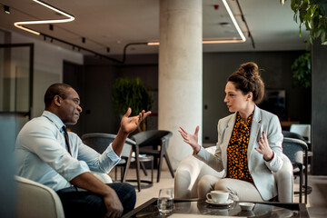 Two young and diverse business colleagues having a conversation in the hotel cafe or bar
